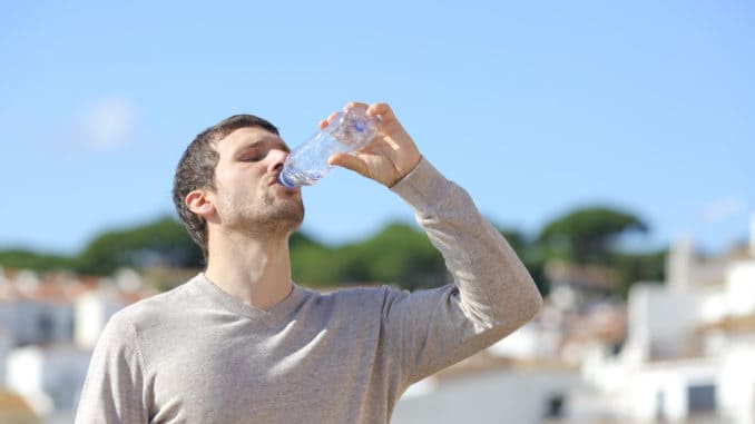 Casual adult man drinking bottled water standing in a rural town a sunny day