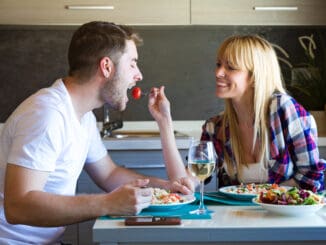 Shot of happy young couple enjoying lunch while women is feeding her boyfriend in the kitchen at home.