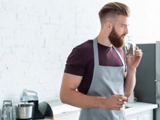 handsome bearded young man in apron holding container with cinnamon sticks in kitchen