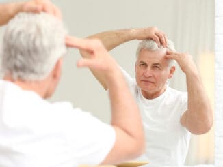 Senior man with hair loss problem looking in mirror indoors