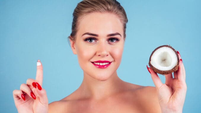 Beautiful woman with perfect skin make-up red lips holding coconut blue background in studio .spa and organic oil cosmetics idea.