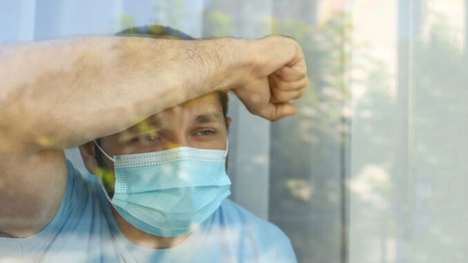 Stressed man in protective mask looking out of window