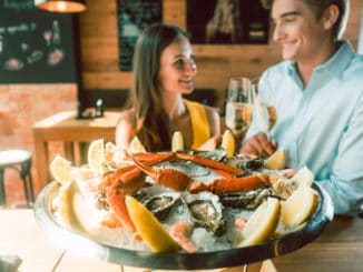 Close-up of fresh oysters and crabs served on ice with slices of lemon at the table of a romantic young couple eating at restaurant