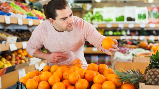 Young man customer looking fresh oranges in fruit store