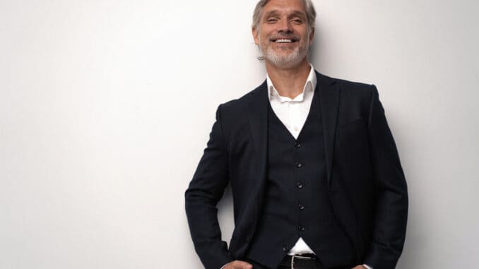 Handsome smiling middle-aged man in suit posing against grey background with copy space