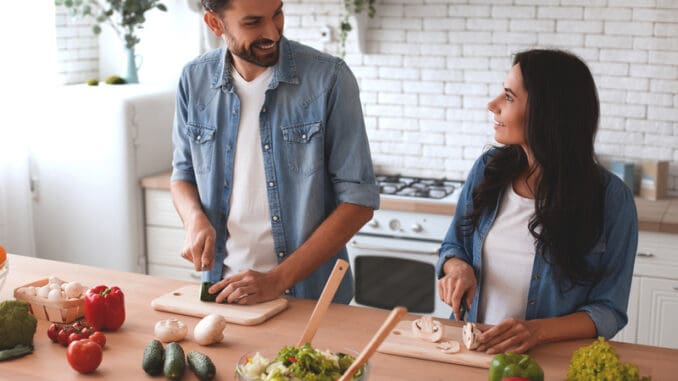 Smiling women and men cooking salad in the kitchen together.