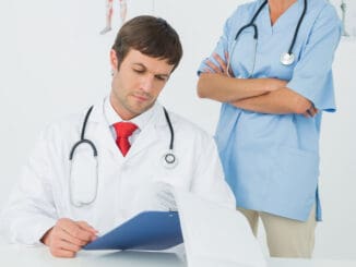 Concentrated male doctor reading reports beside a nurse in the medical office