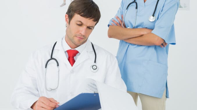 Concentrated male doctor reading reports beside a nurse in the medical office