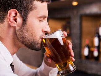 Side view of handsome young man drinking beer while sitting at the bar counter