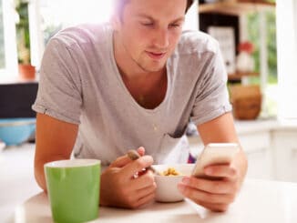 Man Eating Breakfast Whilst Checking Mobile Phone