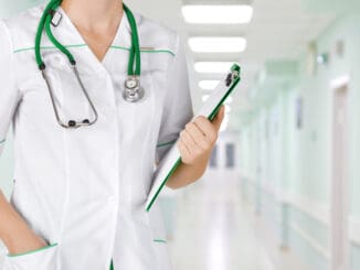 Female medical doctor with clipboard standing over blurry hospital background.