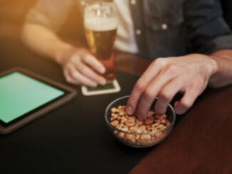 People, leisure and technology concept - close up of man with tablet pc computer drinking beer and eating peanuts at bar or pub