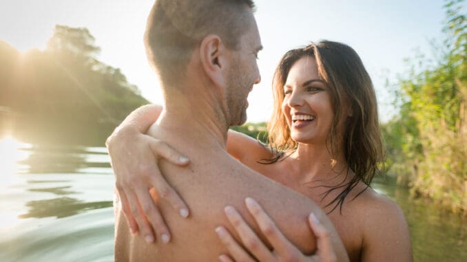 Smiling nude couple hugging in the lake on sunny day